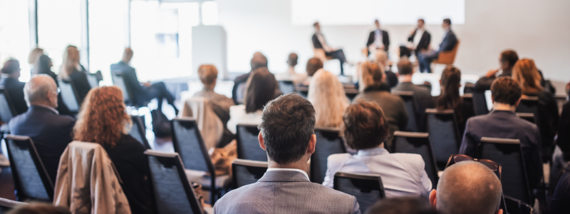 pessoas em um evento empresarial assistindo 4 pessoas realizando a apresentação