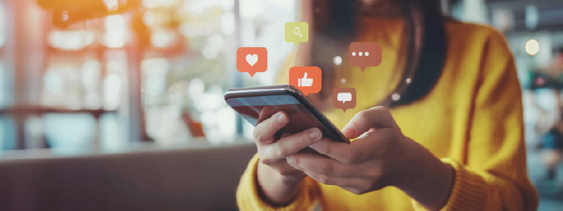 Mulher com camiseta amarela segurando um smartphone e interagindo com redes sociais